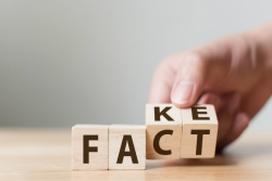 A hand changing the last two letters of the work FAKE to the word FACT