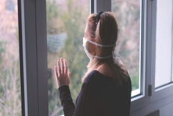 woman in mask looking out the window