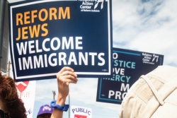 Person holding a sign that reads REFORM JEWS WELCOME IMMIGRANTS