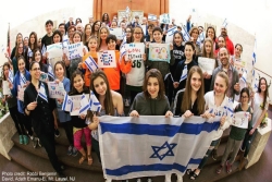 Large congregational group holding the Israeli flag and WE LOVE ISRAEL signs while standing on a synagogue bimah