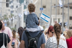 Small child holding an Israeli flag being carried on his father's shoulders