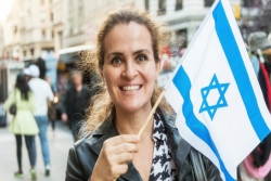 Smiling woman standing outside and waving a small Israeli flag
