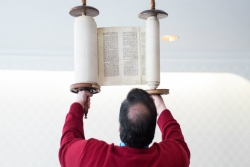 Man in a red sweater facing away from the camera while holding the Torah above his head 