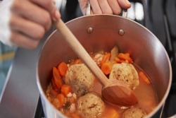 Hand stirring a pot of matzah ball soup