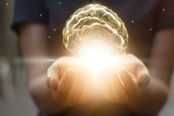 Background figure gently holding an image of the brain on a bed of light in open palms of the hand