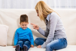 Mother and preschool child on a couch; mother scolding and pointing her finger at the child