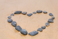 Flat black stones placed on the sand to form an open heart