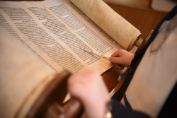 Open Torah scroll with reading pointing a silver yad at the text