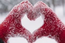 Hands in snow-covered red gloves forming a heart
