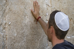 Man in a kippah with his back to the camera and his hand on the Western Wall
