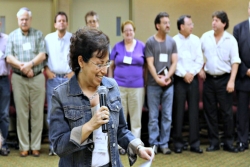 Woman laughing while holding a microphone and speaking in front of a small group 
