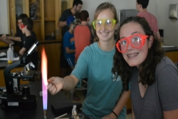 Two girls wearning fluorescent safety goggles and working with a Bunsen burner