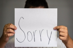 Boy holding paper sign in front of his face that says Sorry.