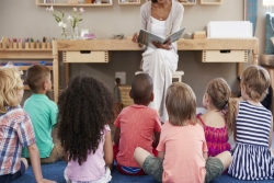 Young children sitting on the floor listening to an adult woman read a story book