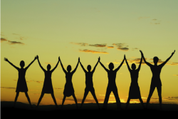 Silhouette of seven women holding hands with arms raised against a sunset