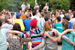 Campers with their arms around one another and their backs to the camera during an outdoor Shabbat service