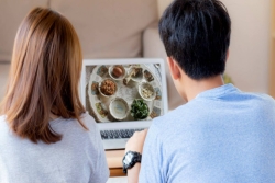 Two people with their backs to the camera as they watch a seder on a laptop screen 