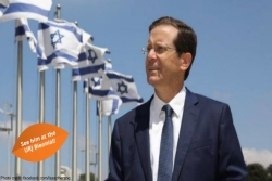 Isaac Herzog standing in front of a row of Israeli flags against a blue sky 
