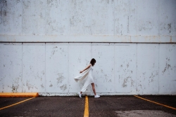 Woman dress in white walking on asphalt against a background of a peeling white wall 