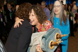 Two women hugging while one holds a Torah