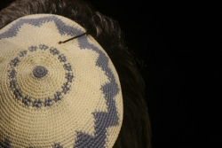 Ivory and blue knit yarmulke pinned to top of dark haired head