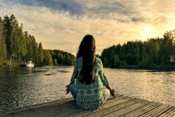 Woman in a yoga pose on a dock facing nature 