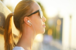 Young woman in profile with a ponytail and sunglasses wearing earbuds