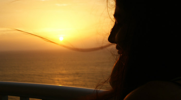 Profile of a woman staring off  into a sunset on the water with her hair blowing around her in the wind