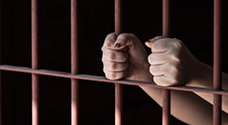 Hands grasp railing behind bars in prison