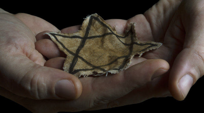 Hands holding a yellow fabric star like the one worn by Jewish victims of the Holocaust
